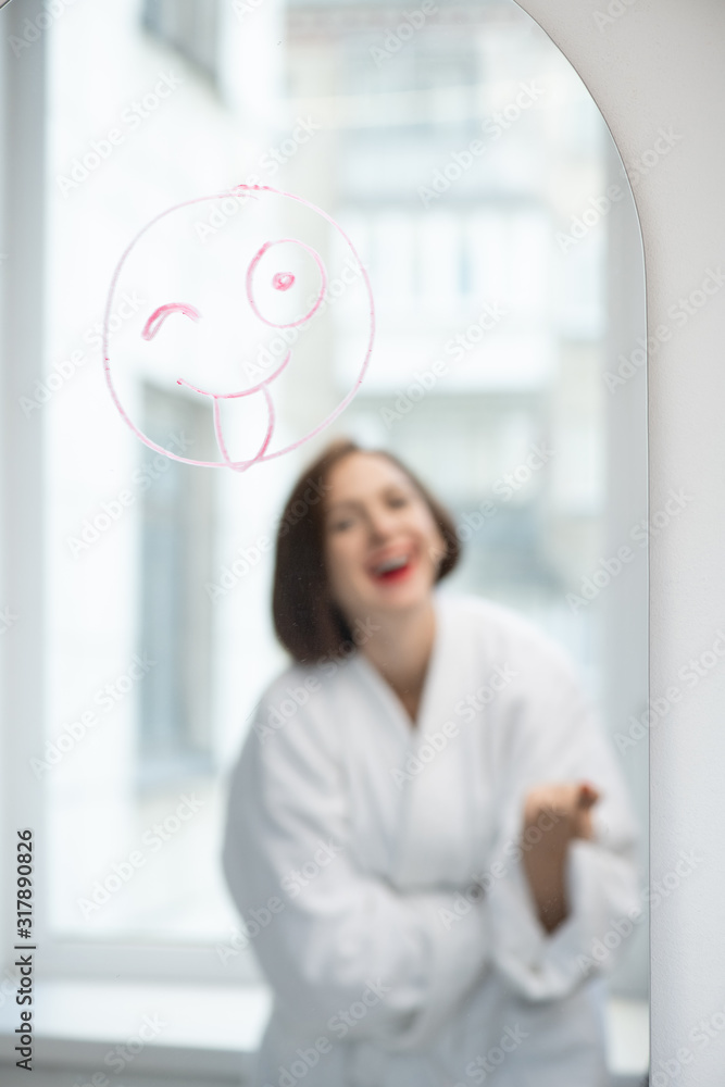 Aufkleber Laughing girl standing in front of mirror with funny face drawn with lipstick