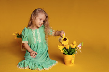 Cute cheerful girl in a green dress on a yellow background holds tulips in her hands and laughs merrily.