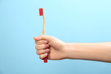 Woman holding bamboo toothbrush on light blue background, closeup