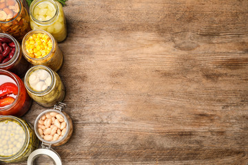 Glass jars with different pickled vegetables on wooden table, flat lay. Space for text