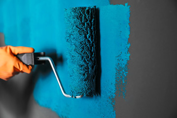 Woman painting grey wall with blue dye, closeup