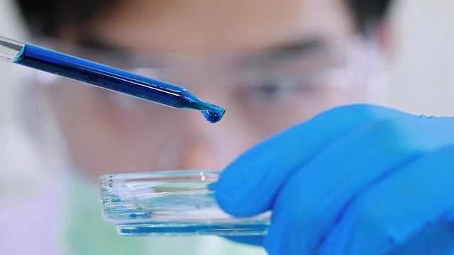 Handsome Asian scientist dropping blue liquid into test tube for his experiment, concept in laboratory room.