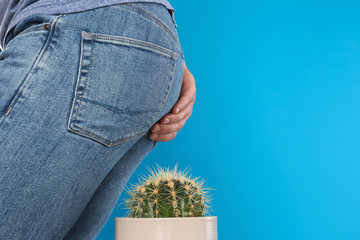 Man sitting down on cactus against light blue background, space for text. Hemorrhoid concept