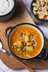 Pumpkin soup in a bowl with crackers and seeds on a gray background close-up