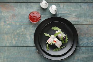 Delicious rolls wrapped in rice paper on light blue wooden table, flat lay