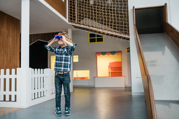 Obraz premium Little boy in casualwear looking through binoculars while standing on play area