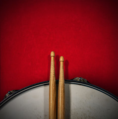 Close-up of two wooden drumsticks and an old metallic snare drum on a red velvet background with copy space. Percussion instrument