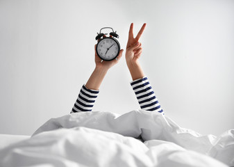 Woman with alarm clock lying in bed, closeup. Morning time