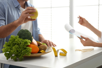 Young nutritionist consulting patient at table in clinic, closeup
