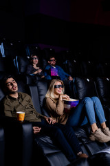 Tired guy sleeping in armchair in cinema while his girlfriend enjoying movie