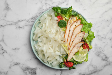 Tasty cooked rice noodles with chicken and vegetables on white marble table, top view