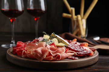 Tasty prosciutto with other delicacies served on wooden table, closeup