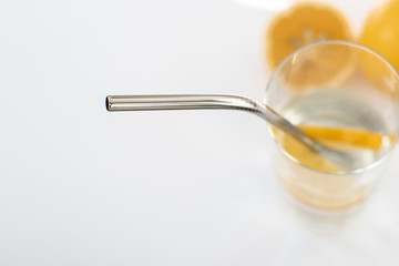 Reusable Metal Straws with Portable Case - Stainless Steel, Eco-Friendly Drinking Straw Set with  Cleaning Brushes. A glass of water with a metal drinking straw. Yellow lemons on a white background.