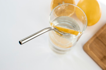 Fototapeta na wymiar Reusable Metal Straws with Portable Case - Stainless Steel, Eco-Friendly Drinking Straw Set with Cleaning Brushes. A glass of water with a metal drinking straw. Yellow lemons on a white background.