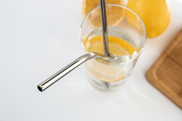Reusable Metal Straws with Portable Case - Stainless Steel, Eco-Friendly Drinking Straw Set with  Cleaning Brushes. A glass of water with a metal drinking straw. Yellow lemons on a white background.