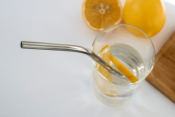 Reusable Metal Straws with Portable Case - Stainless Steel, Eco-Friendly Drinking Straw Set with  Cleaning Brushes. A glass of water with a metal drinking straw. Yellow lemons on a white background.