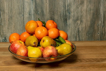 Apples, pears and tangerines in a plate on a wooden background.