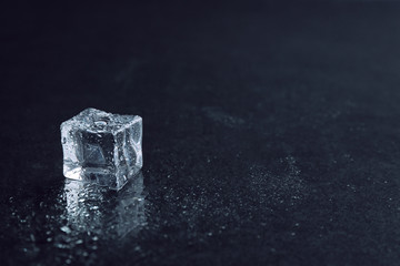 Crystal clear ice cube with water drops on black background. Space for text