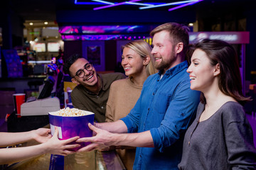Two happy young couples buying popcorn by cashier counter before movie