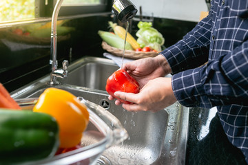 Young man washing vegetables for salad in the kitchen. Vegetables in the sink on kitchen. Fresh vegetables. Homemade