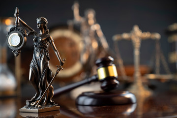 Law and justice theme. Judge’s gavel, Themis  statue, scale, hourglass and old clock on the shining wooden brown table and the gray background.