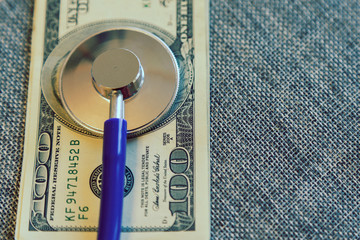 Financial checkup: Stethoscope on pile of U.S. hundred dollar bill on grey background. financial wellness. toned. vertical photo