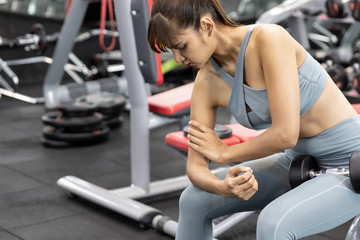 Asian young woman having arm pain after workout at the gym. painful during exercise training dumbbell.