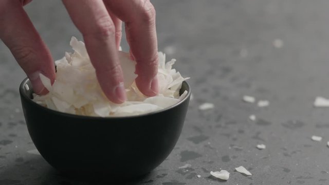 Slow motion man hand takes coconut chips from black bowl on terrazzo surface