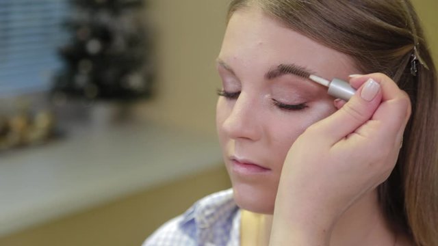 Professional makeup artist paints eyebrows to the client with a special brush.