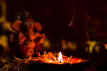 close up of glowing earthen lamp against blurry ganesha statue with dark background. hinduism concept.