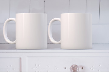 Fototapeta na wymiar White Mug Mockup with 2 mugs, on a white dresser. Perfect for businesses selling mugs, just overlay your quote or design on to the image.