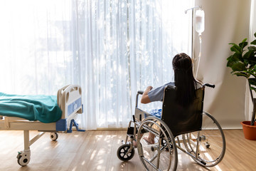 Asian woman patient sitting in the wheelchair at hospital room.