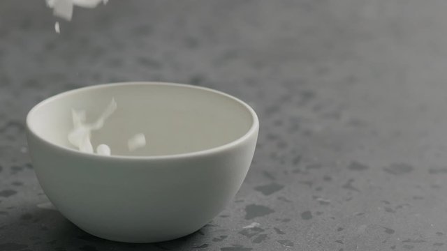 Slow motion coconut chips falls into white bowl on terrazzo surface