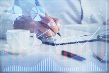 Double exposure of man's hands writing notes of stock market with forex chart.