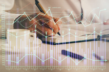 Double exposure of man's hands writing notes of stock market with forex chart.