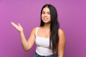 Young teenager Asian girl over isolated purple background holding copyspace imaginary on the palm