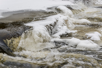 ice and snow on cascades of old broken weir on a river