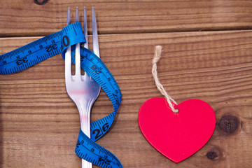 fork with rolled tape measure and heart shaped label, diet and health concept
