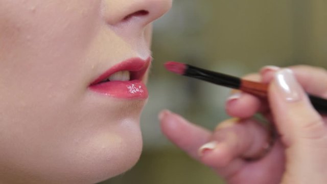 Professional make-up artist applying lip gloss on client s lips with a brush.