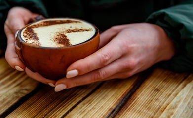 woman hands in gloves hold a cup of hot cappuccino coffee on wooden table background