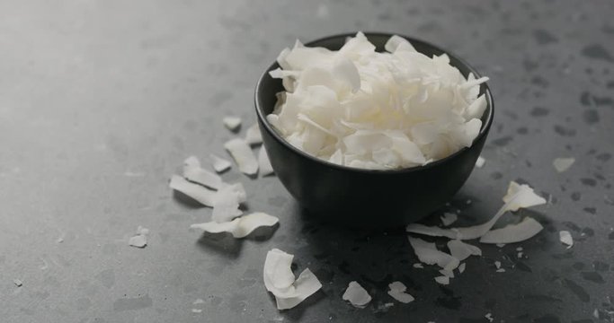 Handheld slow motion of coconut chips in black bowl on terrazzo surface