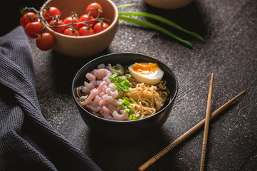 Asian soup with noodles, greens and shrimps on dark background