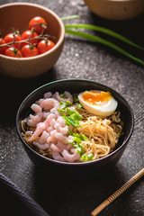 Asian soup with noodles, greens and shrimps on dark background