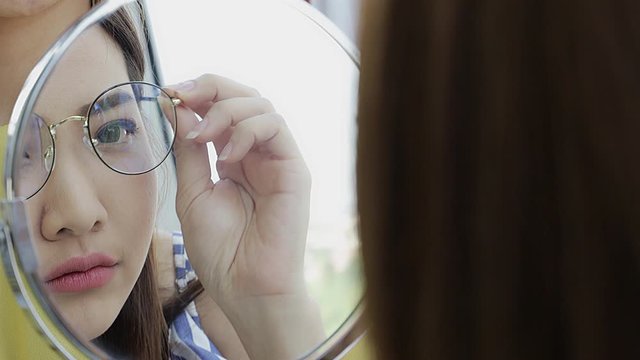 Close up secne video of smiling beautiful Asian woman try glasses in front of mirror for her new look.