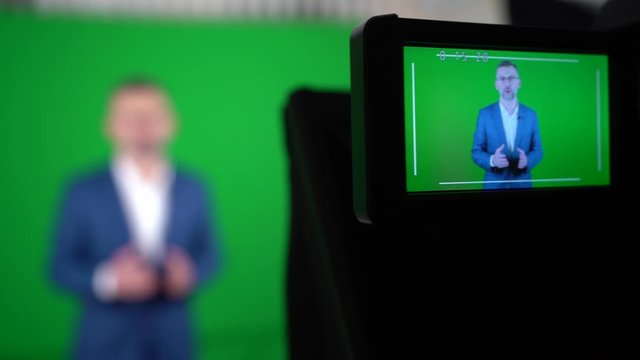 A blogger is recording a video on a green background.  The camcorder is recording a blogger.