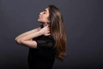 Fototapeta premium Portrait in profile of a confident beautiful girl with natural makeup, holding her hands behind neck, isolated on a grey background.