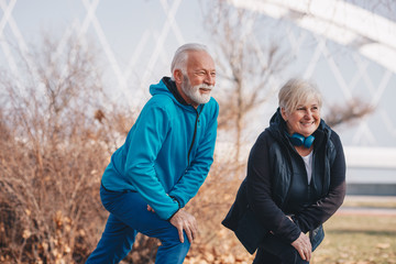A couple of elderly people stretching outdoors.
