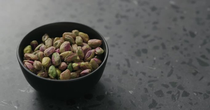 Handheld slow motion peeled pistachios in black bowl on terrazzo surface