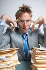 Unhappy businessman frowning between large piles of paperwork stacked on his desk
