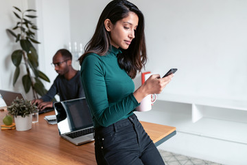 Young indian business woman entrepreneur sending messages with mobile phone in the office.